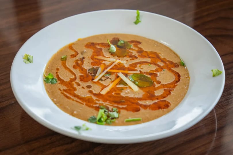 A white bowl of haleem, garnished with cilantro, ginger, and a swirl of chili oil.