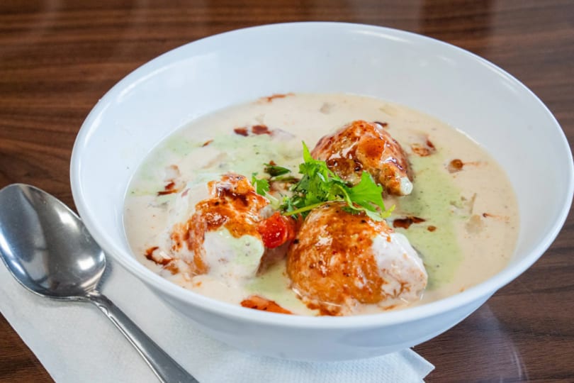 Dahi Vada, a popular Indian snack, served in a white bowl with a spoon on the side.